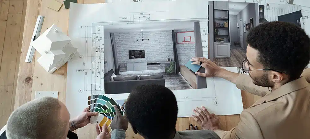 Overview of contemporary designers bending over workplace with blueprint and photos of interior while discussing color palette