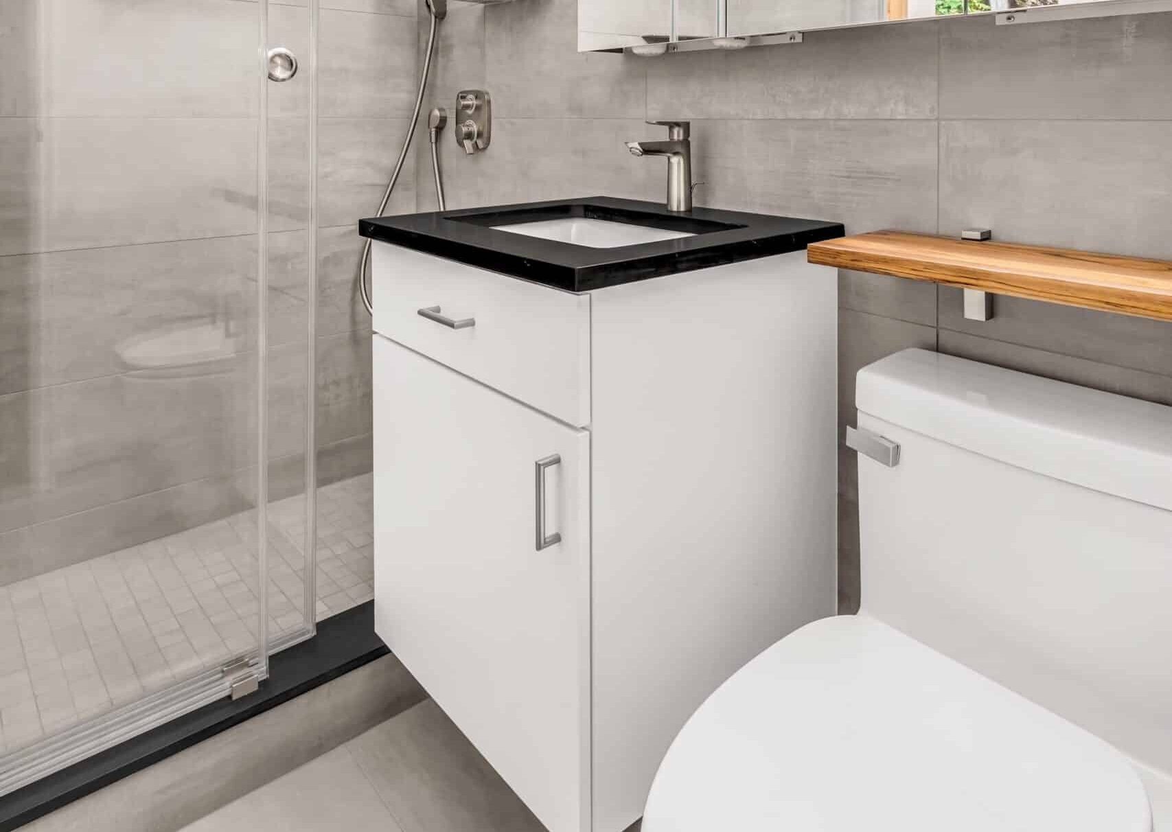 The consistent use of gray tiles on both the floor and walls imparts a sleek and contemporary feel. The spacious shower stands out with its mosaic floor tile, while the black quartz on the shower curb and vanity countertop adds a striking contrast, elevating the overall design.