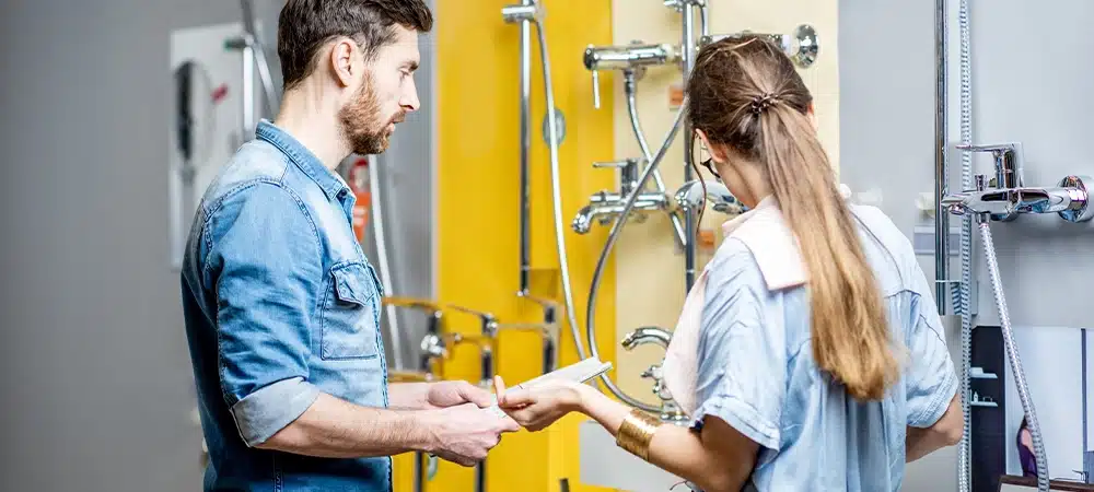 Young couple choosing shower faucet standing near the beautiful showcase of the plumbing shop