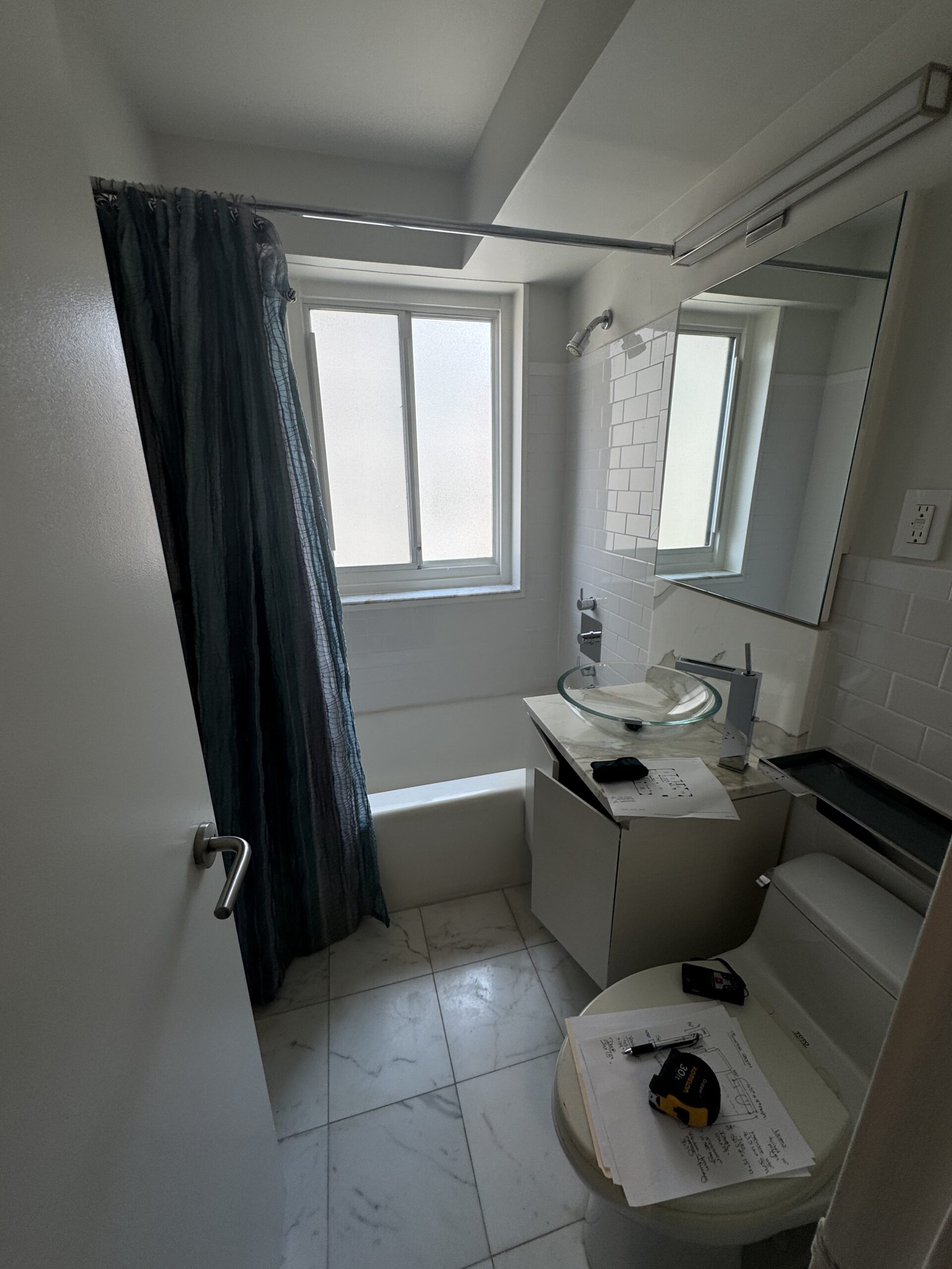 The first guest bathroom at 10 East End Avenue before the renovation, with an alcove tub behind a dark curtain, a vessel sink on a white vanity and a marble-look floor