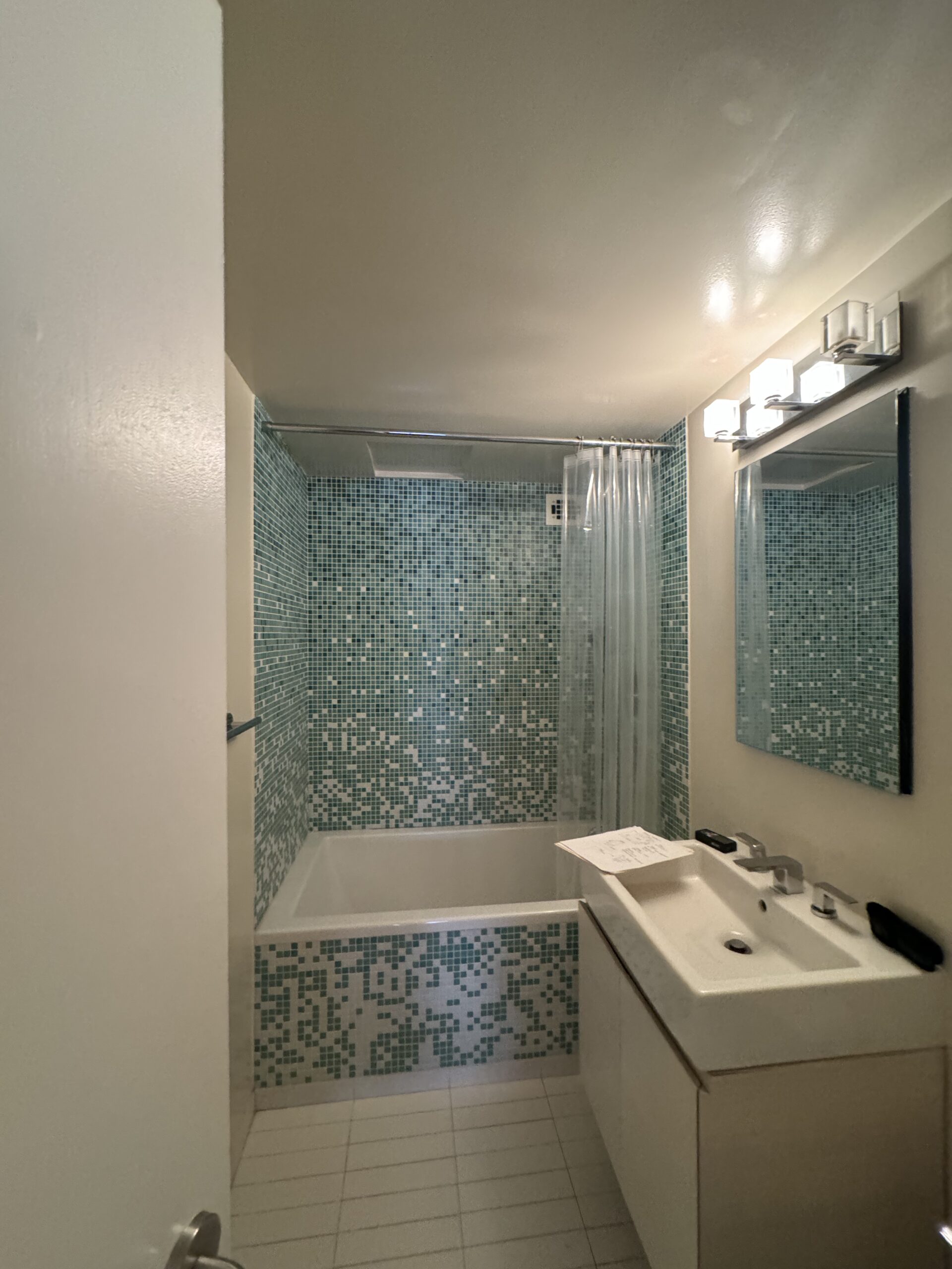 The second guest bathroom at 10 East End Avenue before work, tiled in green glass mosaic with an alcove tub and a trough sink