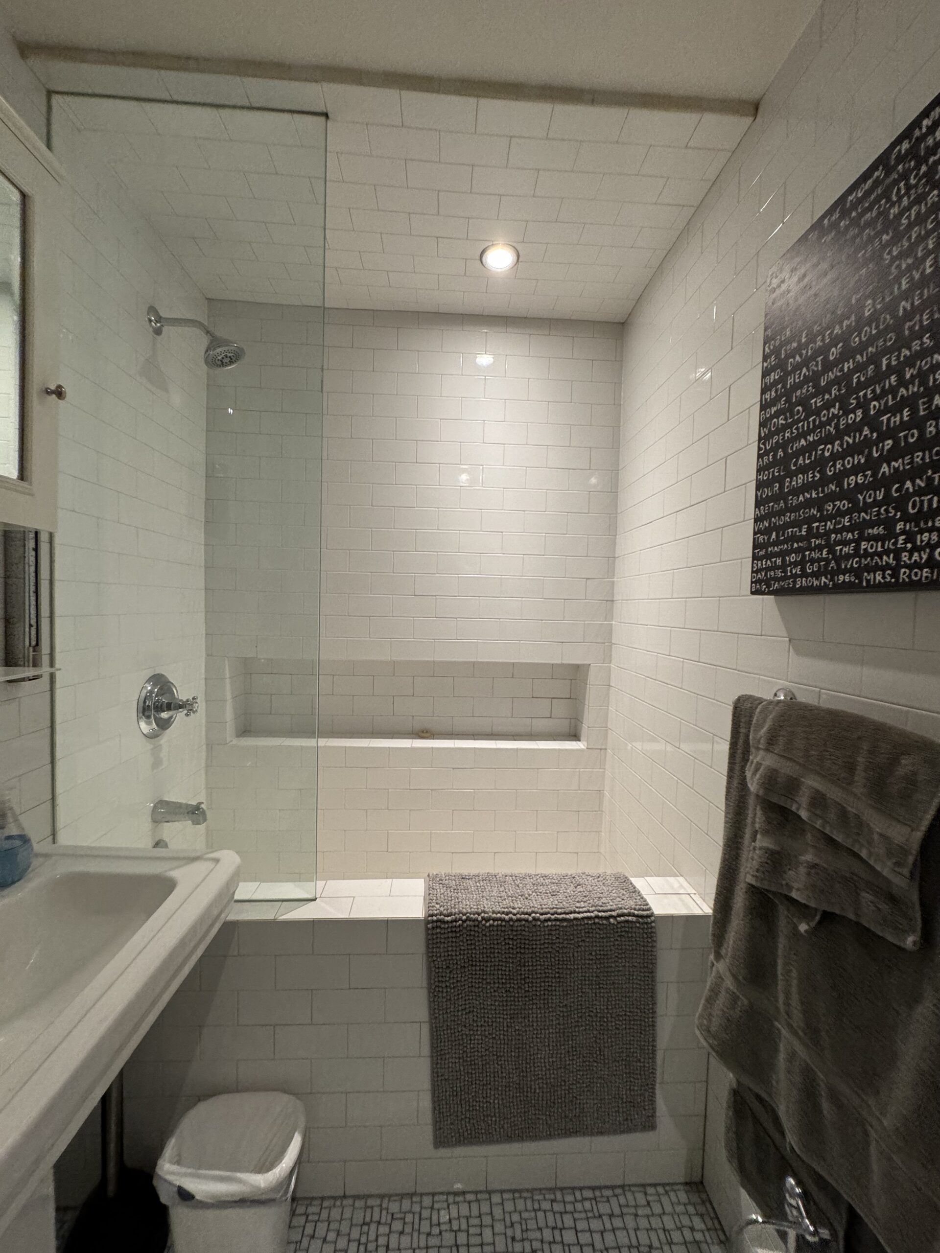 The tub and shower in the powder room before removal, with the mosaic floor and the framed print on the right-hand wall