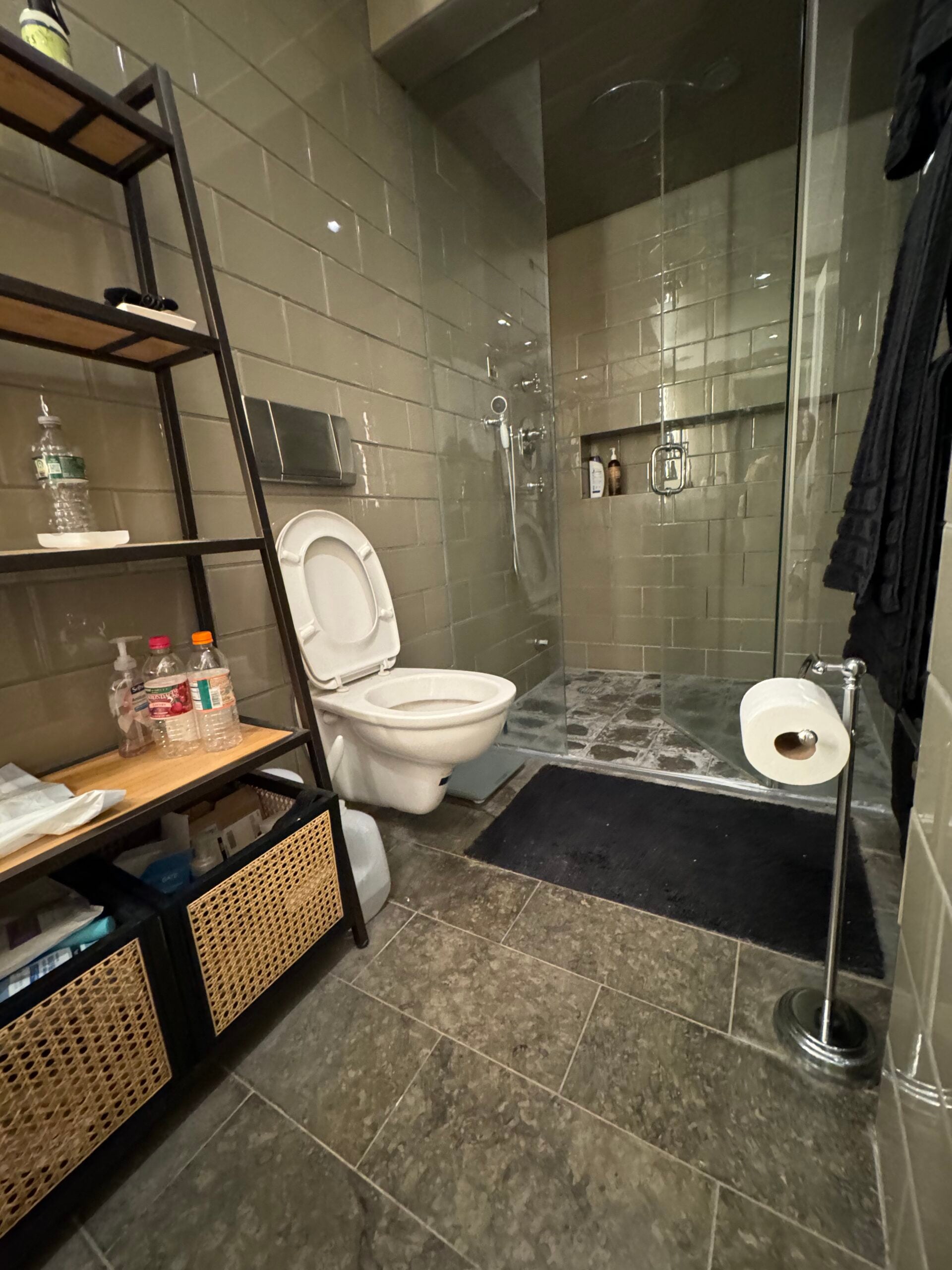 The primary bathroom at 301 East 22nd Street before the renovation, with dark green wall tile, a wall-mount toilet, a pedestal sink and a glass-enclosed steam shower