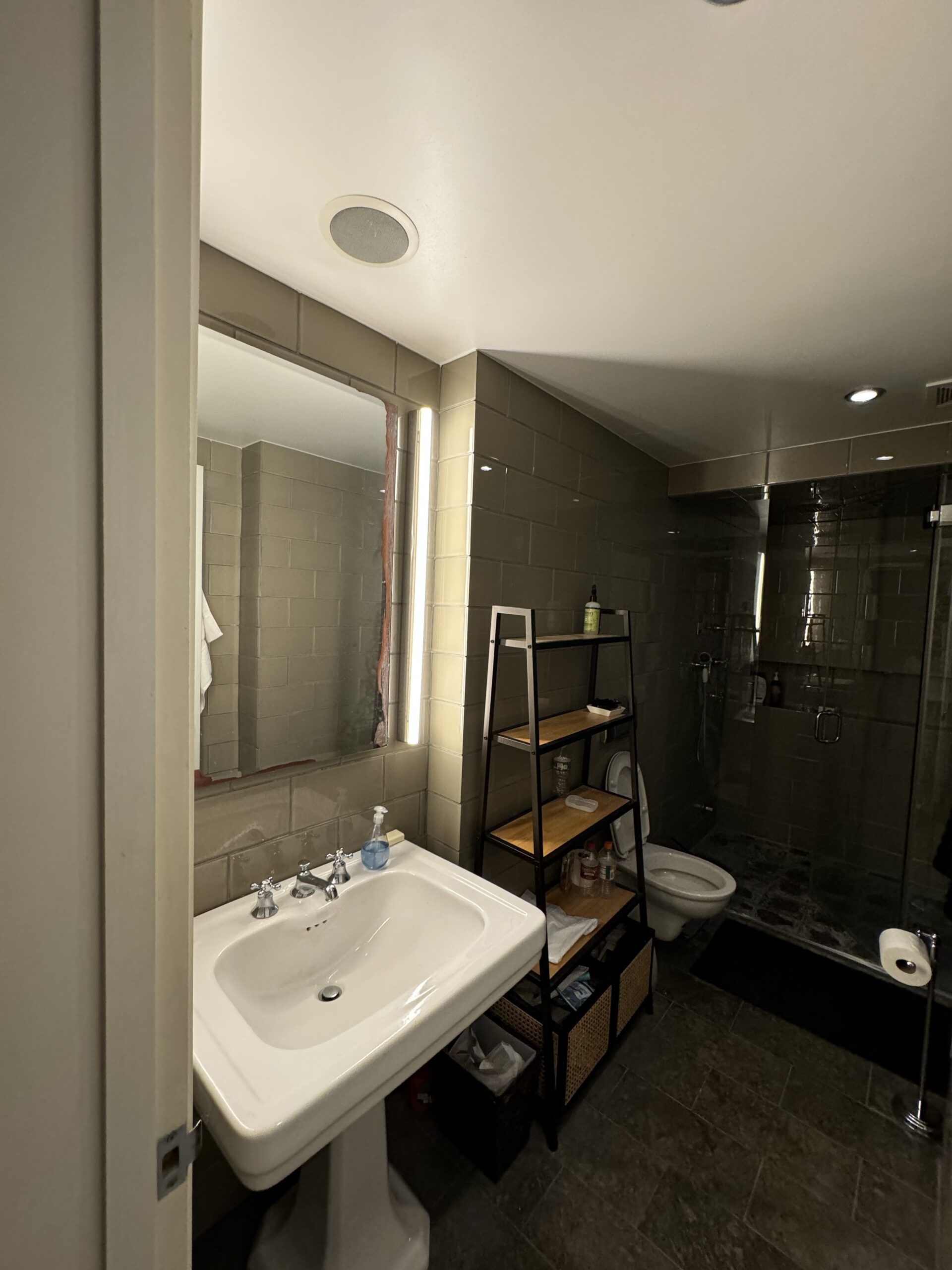 The primary bathroom before work, looking past the pedestal sink and open shelving toward the steam shower