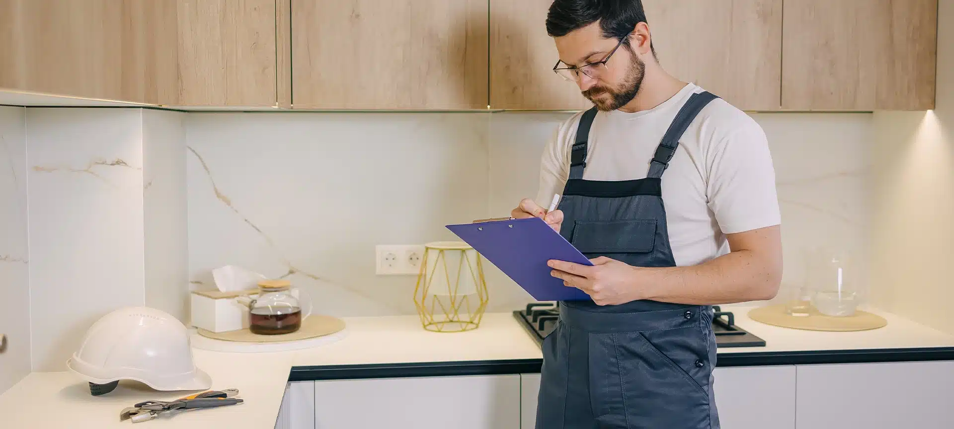 Concerned bearded male in uniform standing in kitchen and describing condition of built in boiling system. Qualified workman providing quality certificate with guarantee for water heating machine.