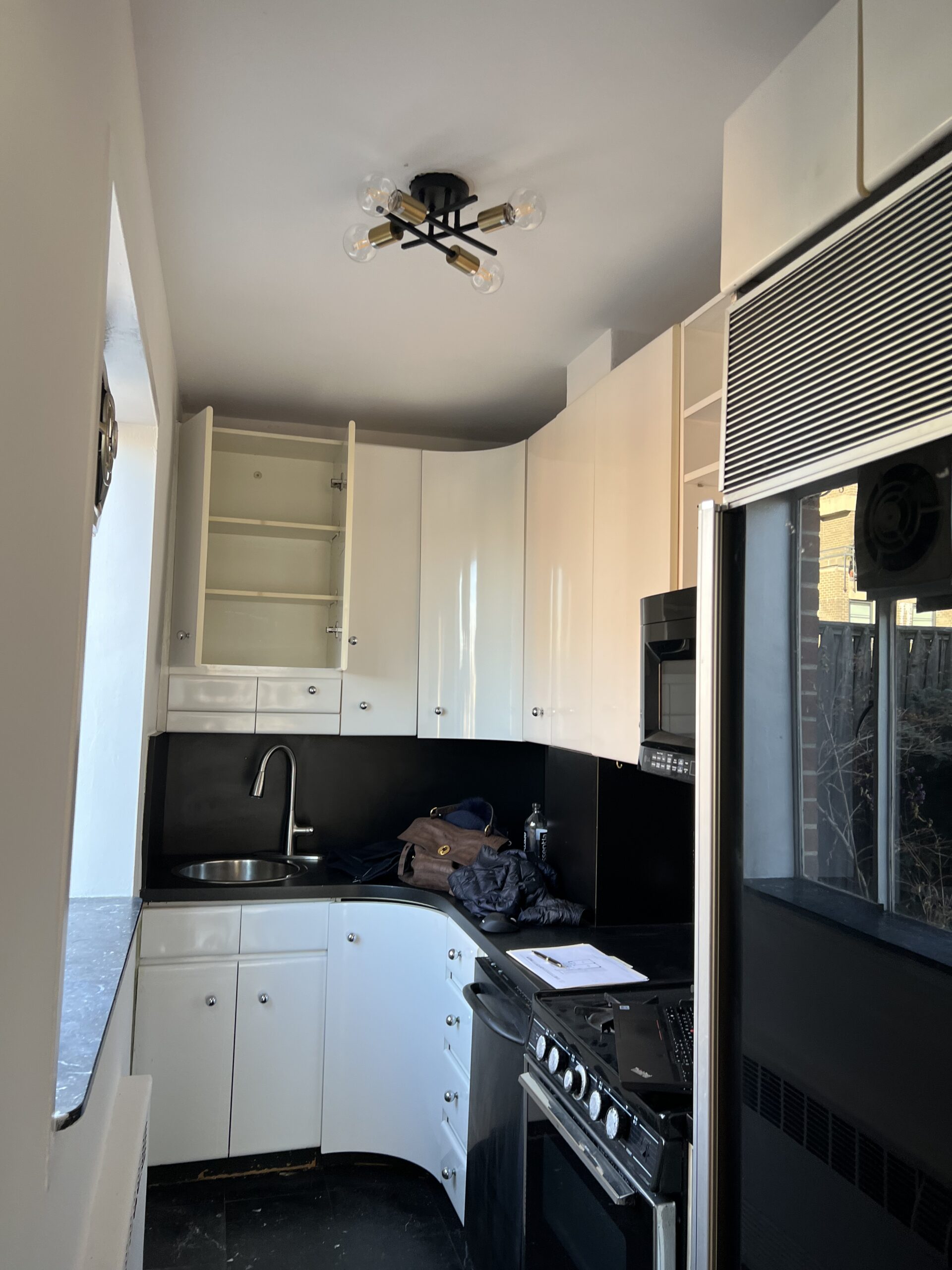 The kitchen at 15 West 12th Street before the renovation, with white gloss cabinets, a black counter and backsplash, two soffits and a black floor