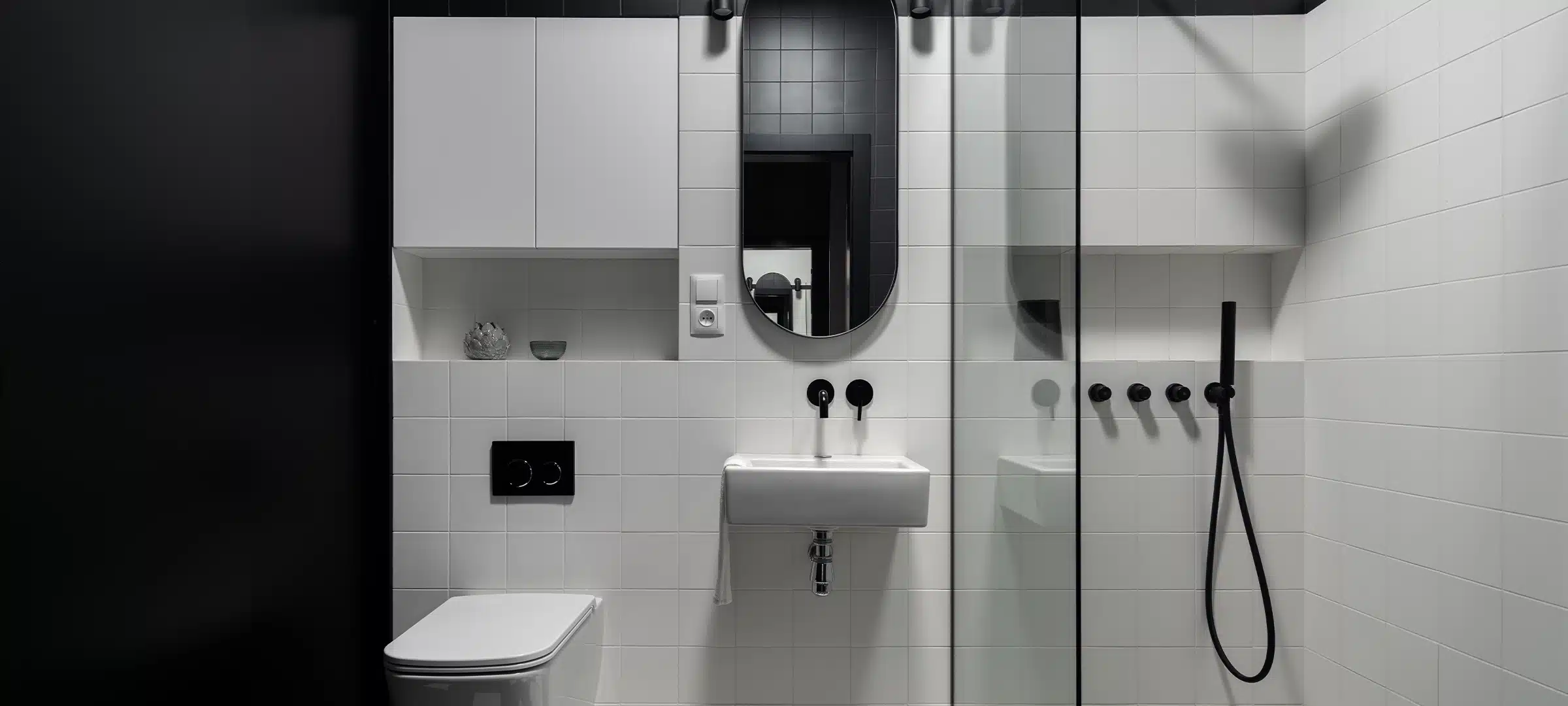 Small and modern black and white bathroom, with shower behind glass wall, oval mirror over washbasin and square toilet