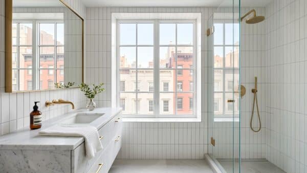 Flawlessly crafted luxury bathroom renovation in a Manhattan pre-war co-op featuring brass fixtures and bright daylight.
