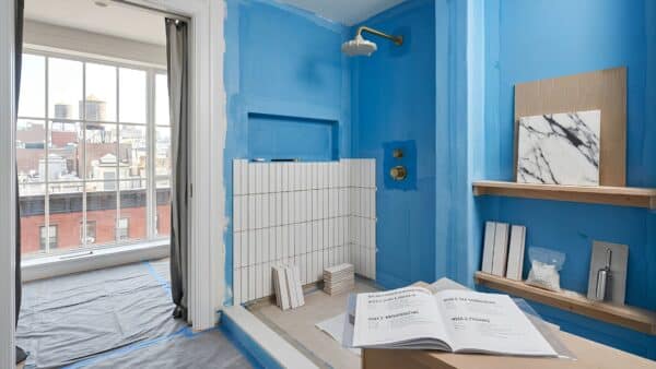 A mid-construction bathroom renovation displaying flawlessly laid vertical white tiles and a brass shower fixture near an Upper West Side window.