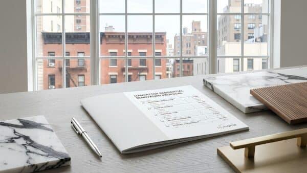 Detailed line-item renovation proposal resting on a desk alongside marble and walnut material samples in front of a Manhattan window.
