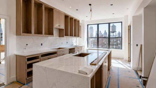 Custom kitchen cabinetry, quartz countertops, and an oversized island being installed in a Manhattan apartment renovation, illustrating the construction and finishing stages that impact NYC kitchen remodel timelines.
