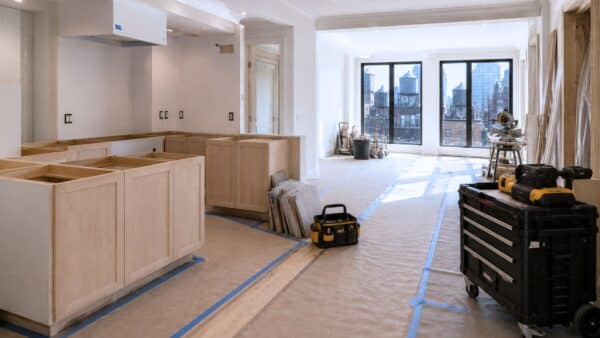 Luxury Manhattan apartment renovation in progress featuring partially installed custom cabinetry, protected hardwood floors, organized contractor tools, abundant natural daylight, and authentic New York City rooftop views.