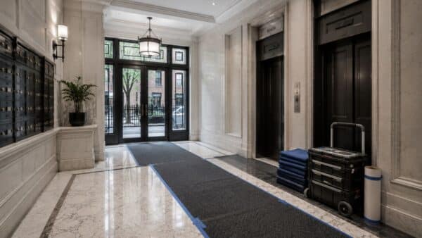 Elegant Manhattan co-op lobby with marble floors, black elevator doors, mailboxes, protective floor coverings, and organized contractor equipment, illustrating the advantages of hiring a contractor familiar with a building's renovation procedures.