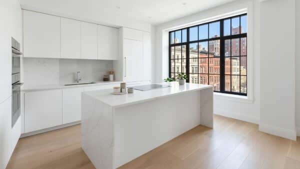 Bright modern kitchen renovation in a Manhattan pre-war apartment with a waterfall quartz island and view of NYC street architecture.