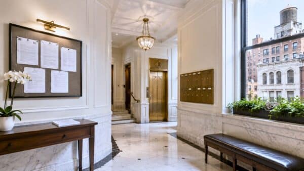 Elegant Manhattan co-op lobby featuring classic architectural details, brass elevator doors, marble finishes, mailboxes, and abundant natural daylight, representing the building approval process that precedes a co-op renovation.