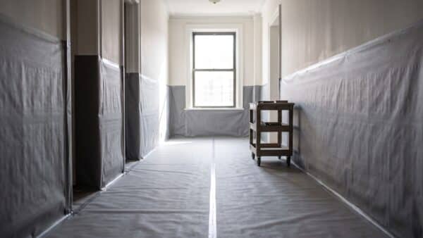 A high-quality photo capturing a pristine classic NYC co-op hallway, meticulously encased in protective gray floor and wall coverings, illustrating respectful renovation logistics.