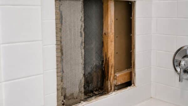 Small shower inspection opening revealing waterproofing and concealed moisture behind bathroom tile.
