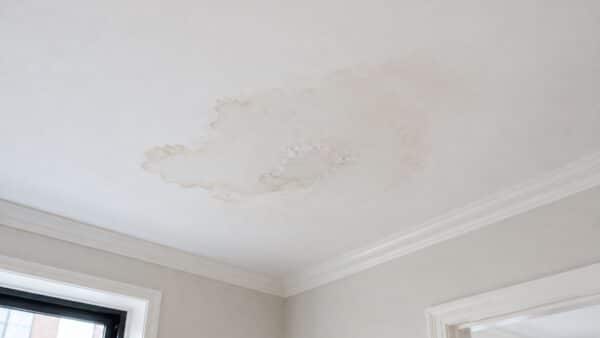 Water stain on the ceiling of an apartment below showing how a bathroom leak can travel through the floor.