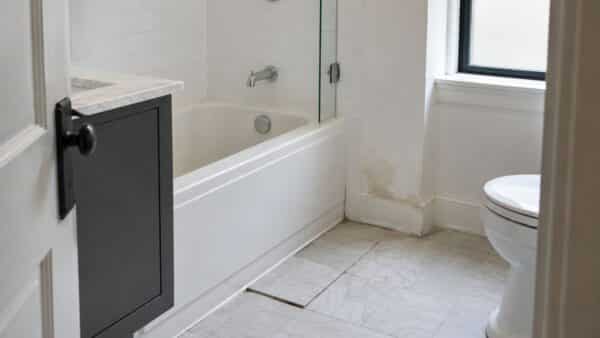NYC bathroom with loose floor tile and subtle water damage near the tub before the source is diagnosed.