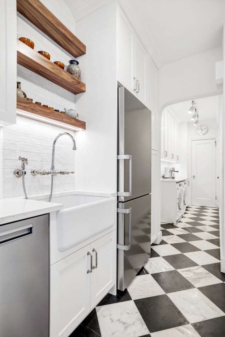 Finished kitchen at 1192 Park Avenue down its length, with a Blanco Cerana apron sink, a Whitehaus wall-mount gooseneck faucet, wood open shelves and the marble chequerboard floor running through to the hall