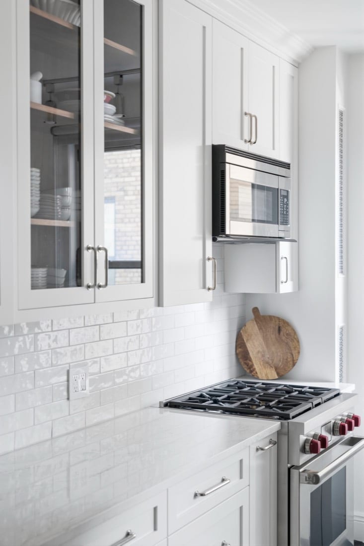 Finished range wall with a Wolf dual fuel range, an Emser Passion Blanco subway backsplash, a Fisher and Paykel microwave built into the cabinetry and a glass-fronted upper