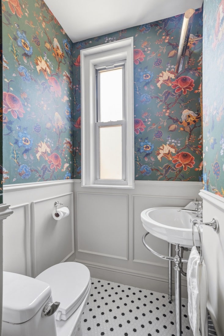 Finished powder room, converted from a bathroom with a drop-in tub, with dark botanical wallpaper above a white panelled wainscot, a wall-hung sink and a black and white mosaic floor