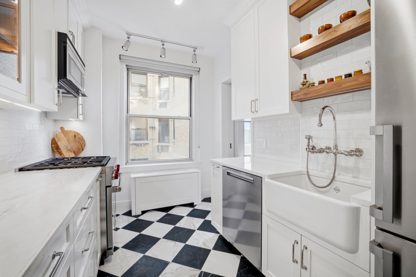 Finished galley kitchen at 1192 Park Avenue with a Tile Bar Avanti Nero Marquina and Calacatta Gold marble chequerboard floor, Plain and Fancy cabinetry, Cambria Everleigh counters, a Wolf dual fuel range under a ducted hood and a Blanco Cerana apron sink with a Whitehaus wall-mount gooseneck faucet
