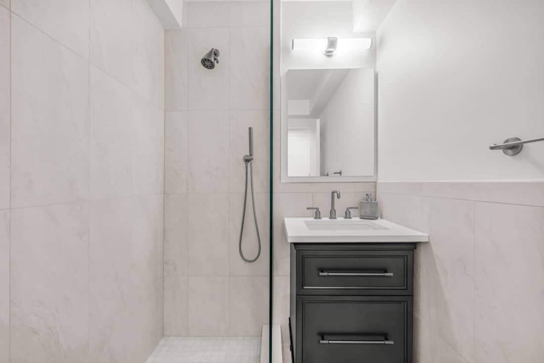 Finished bathroom at 220 Madison Avenue with a Crosswater Fenmore handshower on a slide bar, a thermostatic control, a Kohler slate grey vanity with a Caesarstone Organic White top and a Sofia medicine cabinet