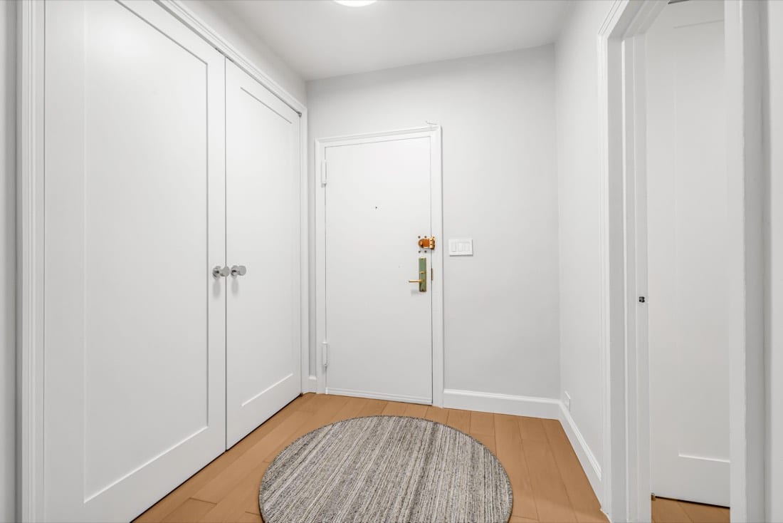 Finished entry hall with Trustile full-height pivot doors in white, a round rug and Terra Legno engineered wood flooring in Natural Nude