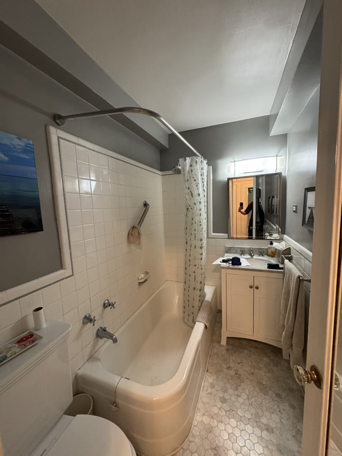 Before renovation: wider view of the original bathroom showing the toilet, tub, vanity and the recessed medicine cabinet