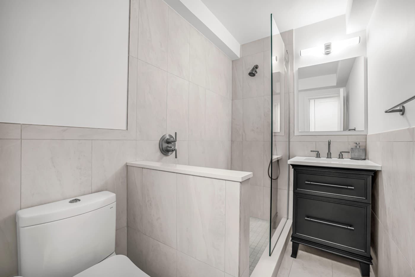Finished bathroom at 220 Madison Avenue with Cancos Paradise Ice porcelain tile run floor to ceiling, a Fleurco shower panel over a lead pan and cement curb, a Kohler slate grey vanity with a Caesarstone Organic White top and Crosswater Fenmore thermostatic controls in graphite
