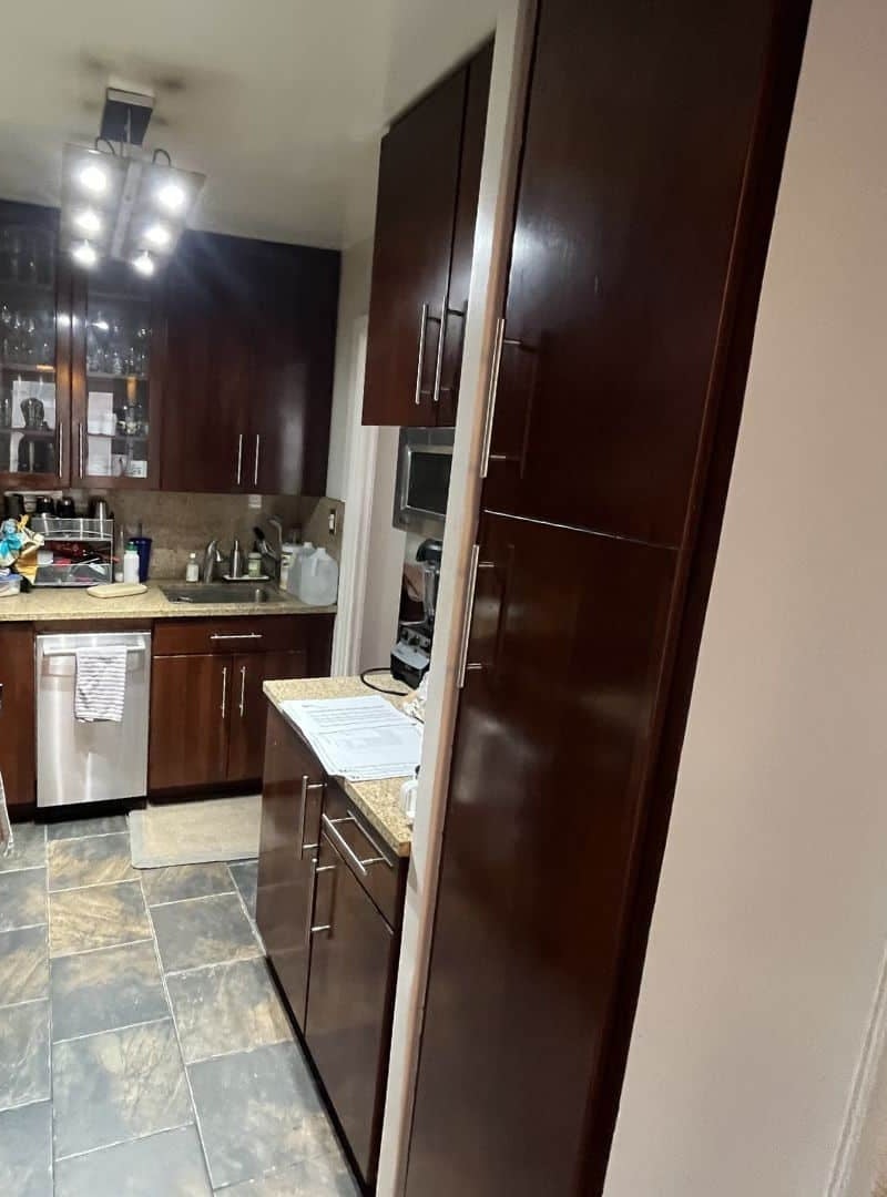 Before renovation: the original galley kitchen at 230 East 79th Street looking toward the range, with dark cherry cabinets, a granite counter and a slate tile floor