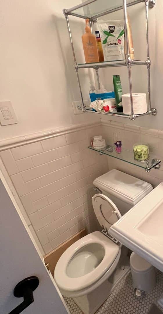 Before renovation: the original guest bathroom at 55 East 9th Street with a pedestal sink, white subway tile to a chair rail, a chrome wall shelf and a toilet