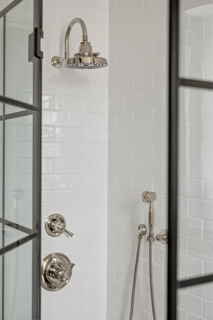 Finished shower interior: a Brizo Invari polished nickel raincan head on an arc arm, a Baliza pressure balance trim and a wall-mount hand shower against Daltile Arctic White subway tile