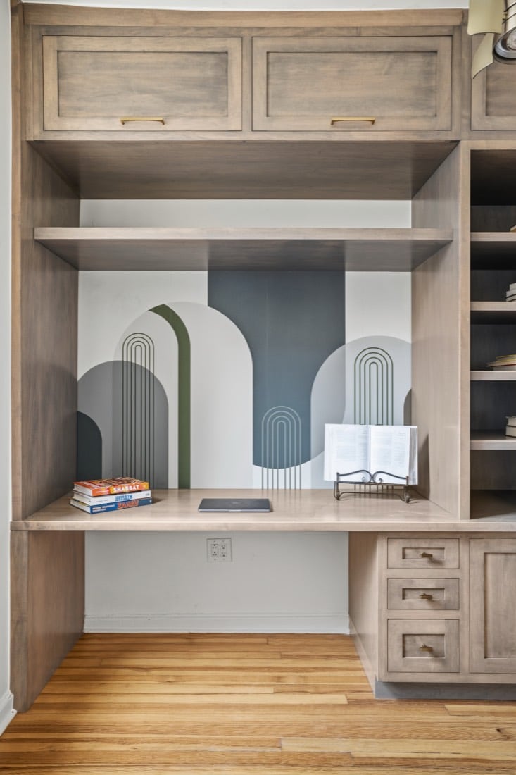 Finished home office built-in in Plain and Fancy Quaker Shaker inset cherry in Platinum, a desk bay with shelves above and drawers below against a painted arch mural