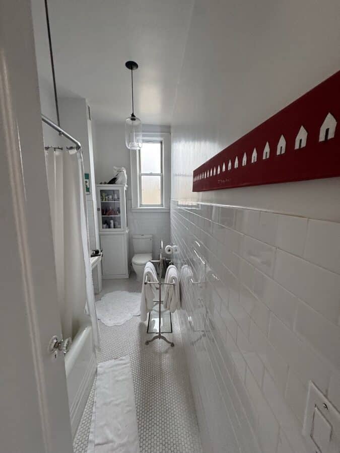 Before renovation: plain white square wall tile, a cast-iron bathtub with a curtain rod and a shower head on a riser, white mosaic floor