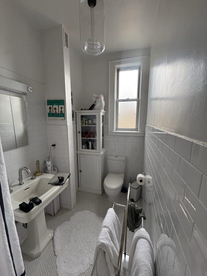 Before renovation: a 24 inch pedestal sink with an exposed trap, a recess-mount medicine cabinet, a toilet and a tall glass-fronted corner cabinet